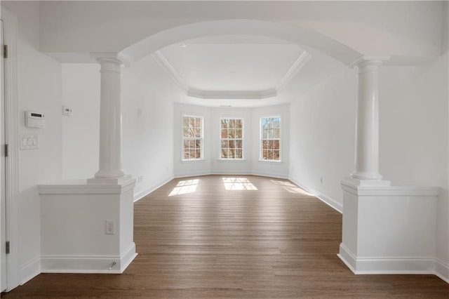 unfurnished room with a tray ceiling, decorative columns, and wood finished floors