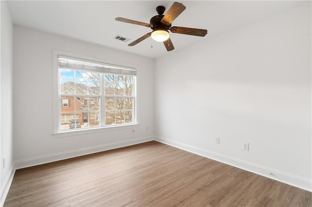 empty room with wood finished floors, visible vents, and baseboards