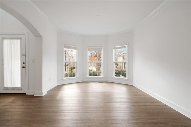 empty room featuring crown molding, arched walkways, and dark wood-style flooring