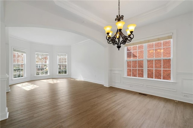 unfurnished room featuring crown molding, a decorative wall, wood finished floors, and arched walkways