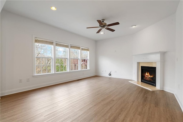 unfurnished living room featuring baseboards, a warm lit fireplace, and wood finished floors