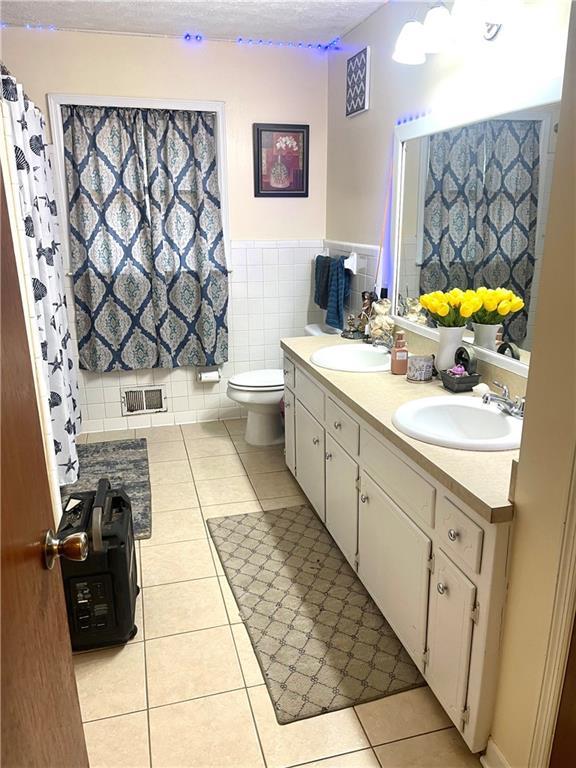 bathroom featuring tile walls, vanity, a textured ceiling, tile patterned floors, and toilet