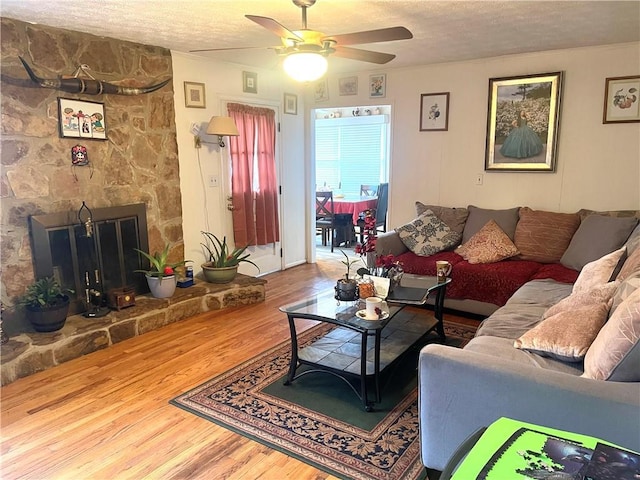 living room featuring a fireplace, wood-type flooring, a textured ceiling, and ceiling fan