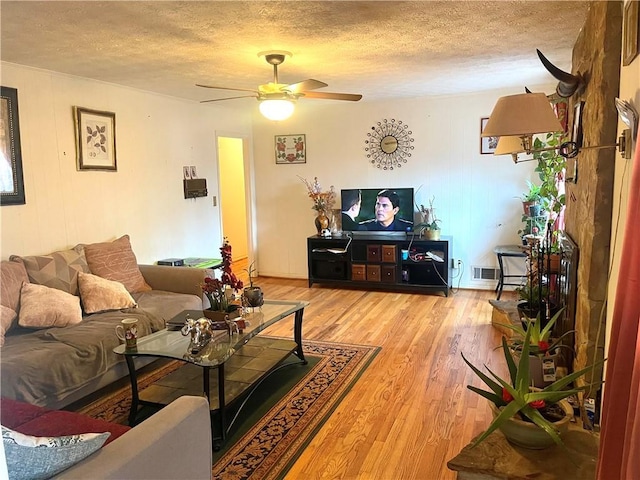 living room with ceiling fan, a textured ceiling, and light wood-type flooring