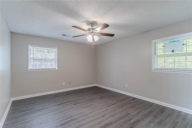 unfurnished room featuring a ceiling fan, dark wood-style flooring, a healthy amount of sunlight, and visible vents