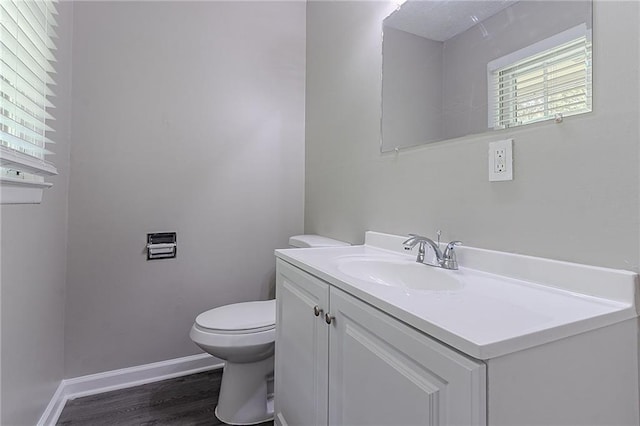 half bathroom featuring toilet, baseboards, wood finished floors, and vanity