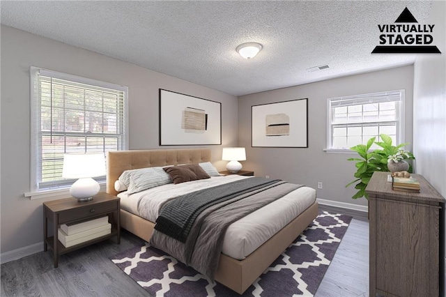 bedroom with a textured ceiling, baseboards, visible vents, and wood finished floors