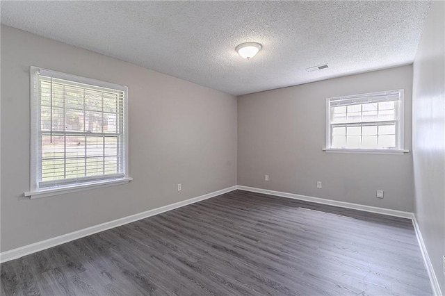 spare room featuring baseboards, dark wood-style flooring, visible vents, and a textured ceiling