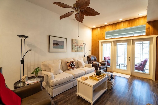 living room with dark wood-type flooring, ceiling fan, and wood walls