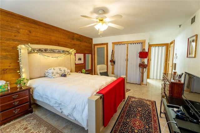 tiled bedroom featuring ceiling fan, a closet, and wood walls