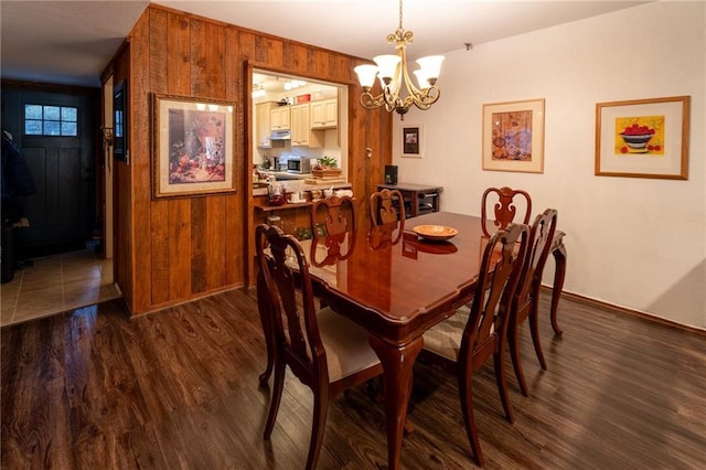 dining room featuring wooden walls, a chandelier, and dark hardwood / wood-style flooring