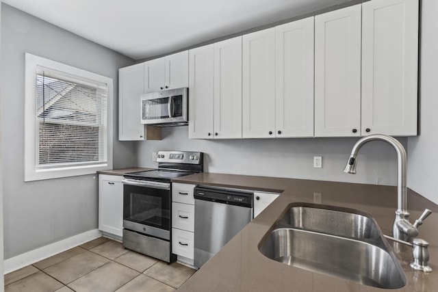 kitchen with light tile patterned floors, dark countertops, appliances with stainless steel finishes, white cabinetry, and a sink