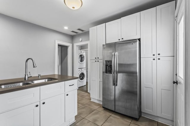 kitchen featuring a sink, light tile patterned flooring, stainless steel fridge, and stacked washer and clothes dryer