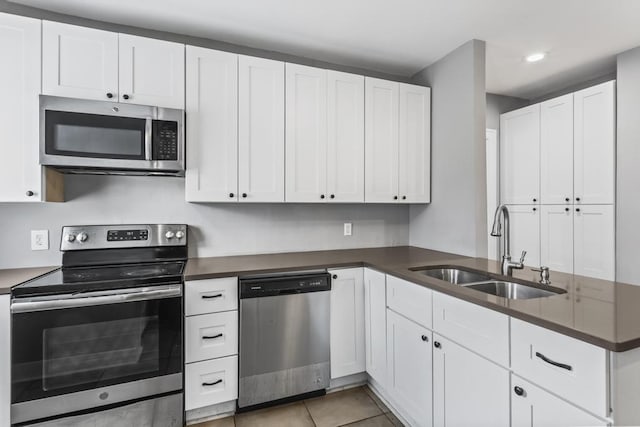 kitchen featuring light tile patterned floors, white cabinets, dark countertops, appliances with stainless steel finishes, and a sink