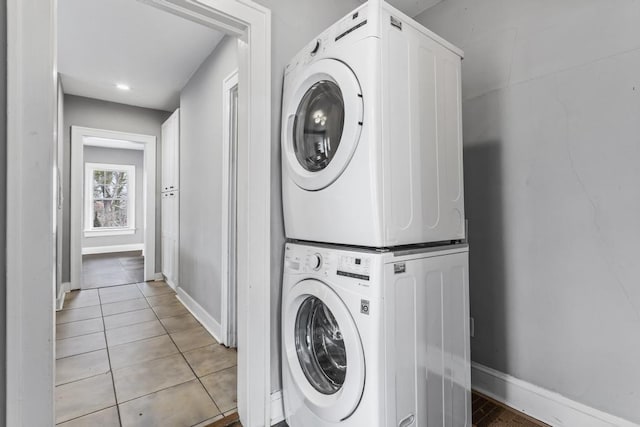 laundry area featuring laundry area, baseboards, stacked washer / drying machine, and light tile patterned flooring