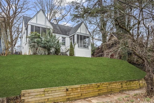 exterior space with a sunroom, roof with shingles, brick siding, and a front lawn