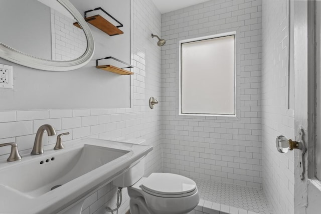 full bath featuring toilet, a sink, a tile shower, a healthy amount of sunlight, and tile walls