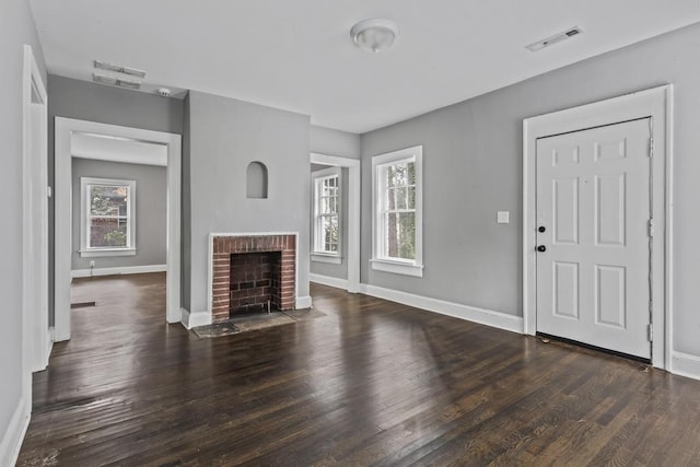 unfurnished living room featuring a healthy amount of sunlight, a brick fireplace, visible vents, and wood finished floors