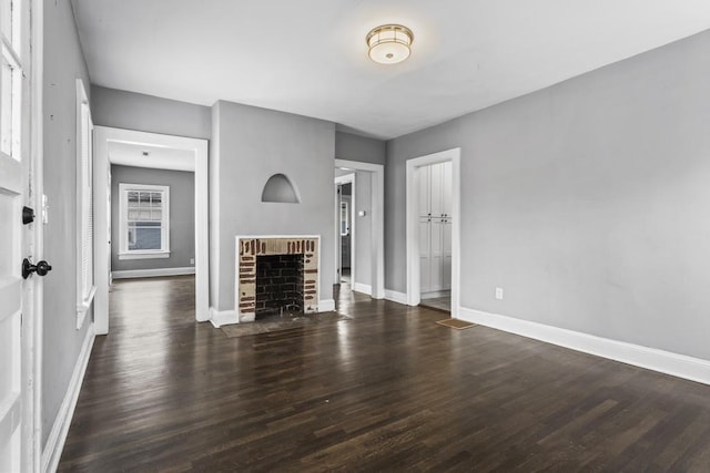 unfurnished living room featuring a brick fireplace, wood finished floors, and baseboards