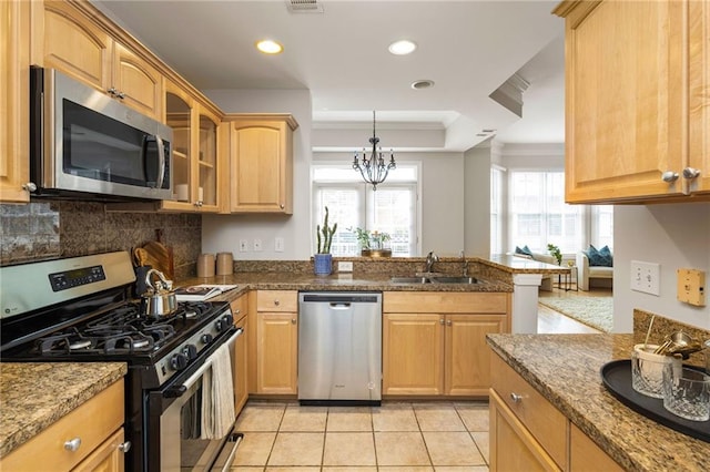 kitchen with appliances with stainless steel finishes, an inviting chandelier, dark stone counters, light tile patterned flooring, and sink