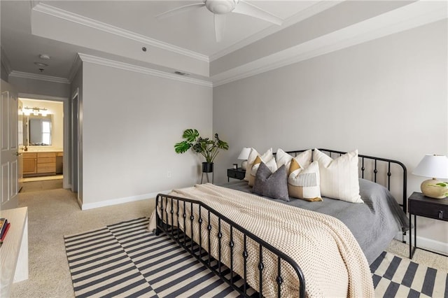 carpeted bedroom with ornamental molding, ensuite bath, a tray ceiling, and ceiling fan