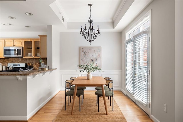 dining room featuring light hardwood / wood-style flooring, ornamental molding, a chandelier, and a raised ceiling