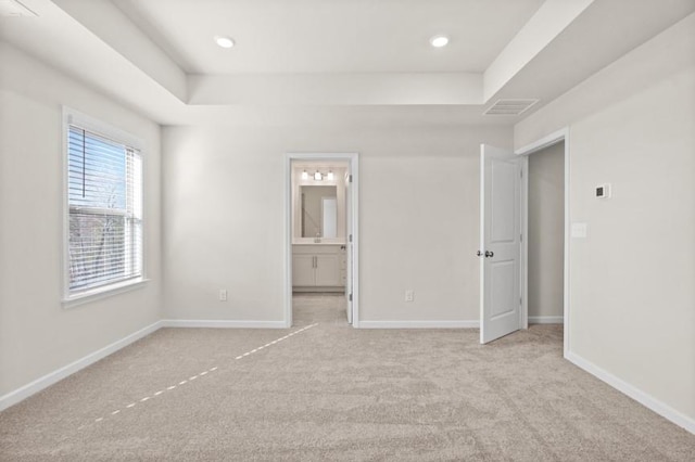 unfurnished bedroom featuring light colored carpet, connected bathroom, and a raised ceiling