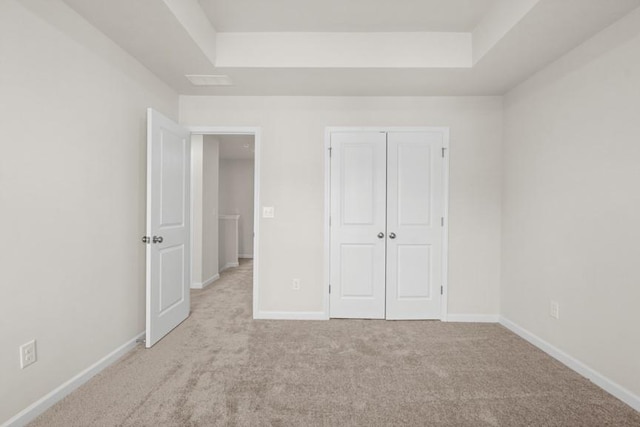 unfurnished bedroom featuring light carpet, a closet, and a raised ceiling