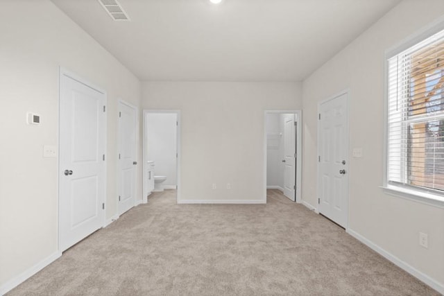 unfurnished bedroom featuring light carpet and ensuite bath