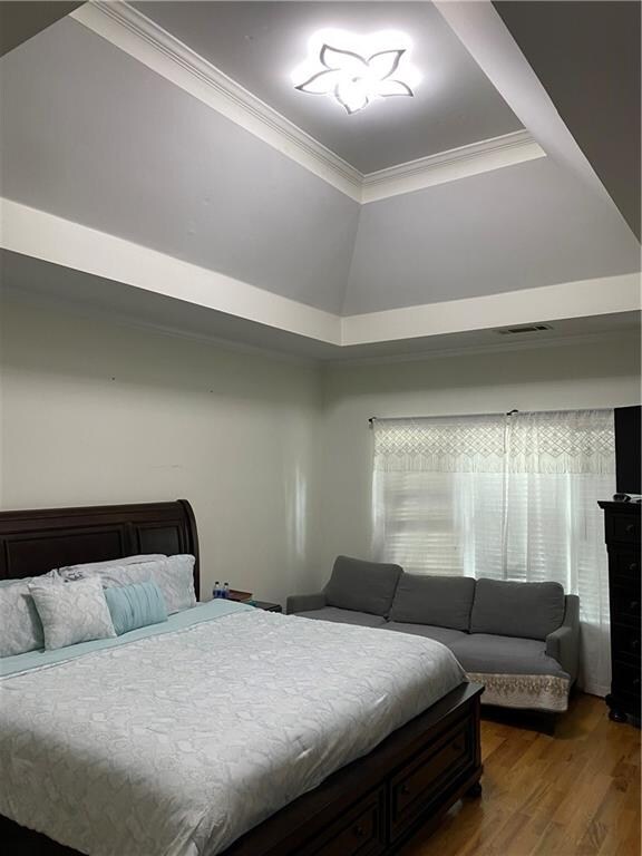 bedroom with wood-type flooring, ornamental molding, and a raised ceiling