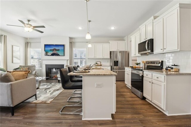 kitchen with a kitchen island with sink, pendant lighting, light stone counters, dark hardwood / wood-style floors, and appliances with stainless steel finishes