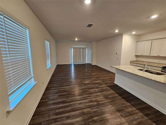 kitchen featuring light stone counters, a sink, visible vents, white cabinets, and dark wood finished floors