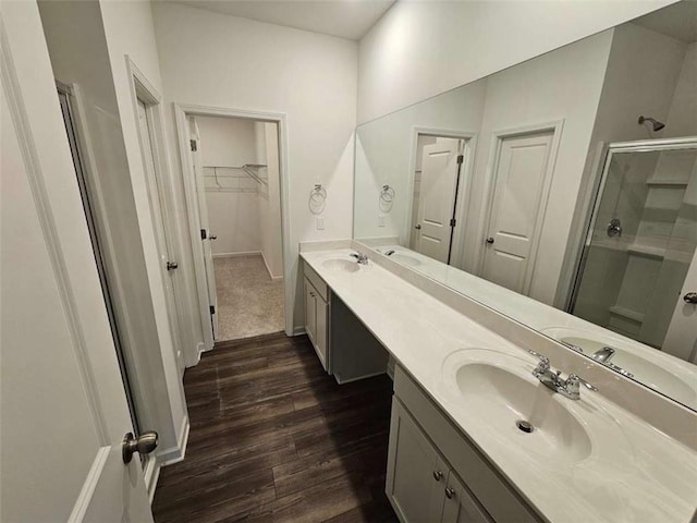 bathroom with a sink, wood finished floors, a shower stall, double vanity, and a walk in closet