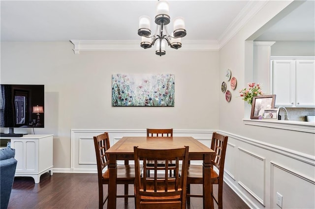 dining space featuring wainscoting, ornamental molding, dark wood-type flooring, an inviting chandelier, and a decorative wall