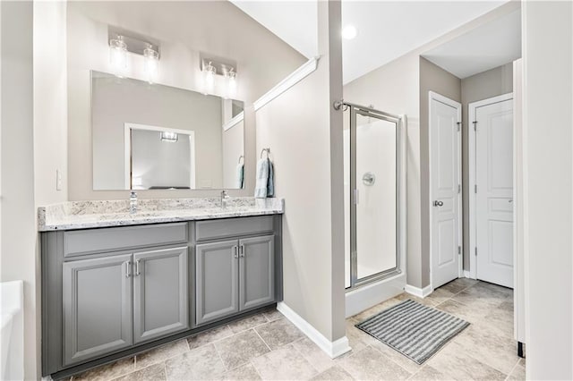 full bath featuring double vanity, a stall shower, baseboards, and a sink