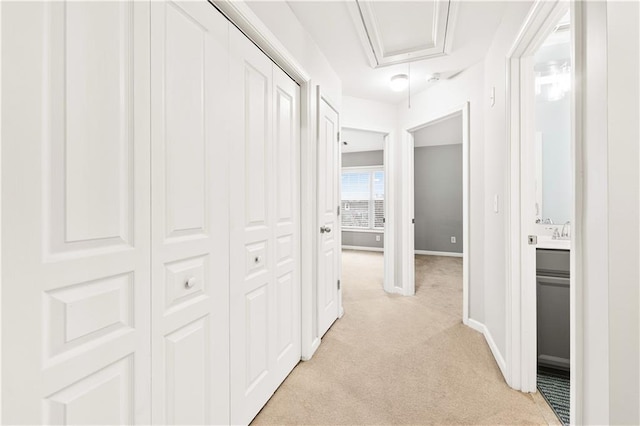 corridor with light carpet, attic access, and baseboards