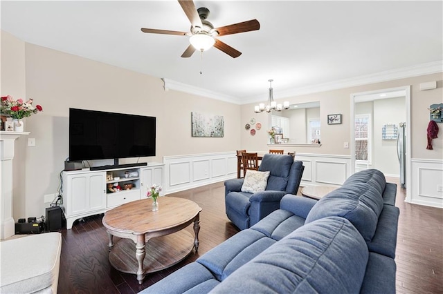 living room featuring a decorative wall, a wainscoted wall, ceiling fan with notable chandelier, ornamental molding, and dark wood-style floors