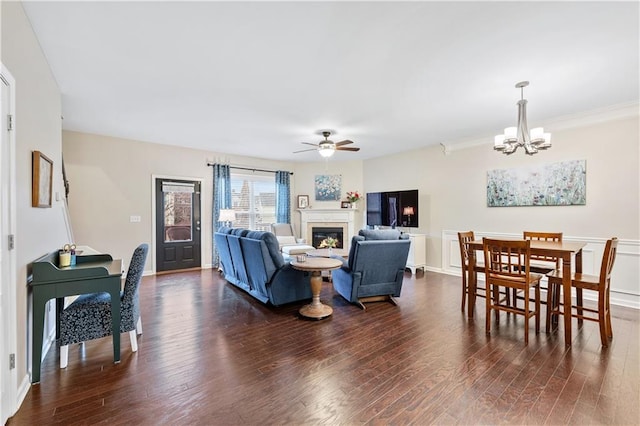 living area featuring dark wood-style floors, ceiling fan with notable chandelier, ornamental molding, and a glass covered fireplace