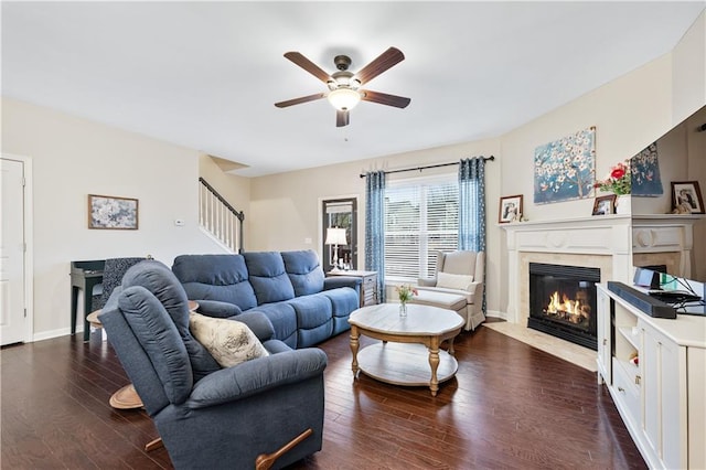 living area with stairs, dark wood finished floors, a ceiling fan, and a high end fireplace