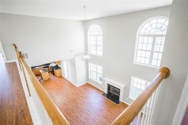 unfurnished living room featuring wood finished floors, a fireplace with flush hearth, ceiling fan, baseboards, and visible vents