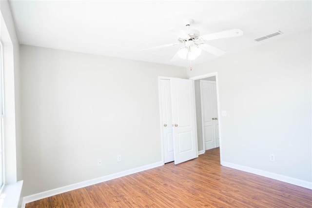spare room with wood finished floors, visible vents, a ceiling fan, and baseboards