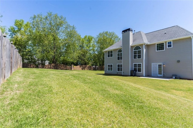 rear view of property featuring fence, a lawn, a chimney, and a patio