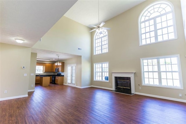 unfurnished living room with dark wood-type flooring, a high ceiling, a healthy amount of sunlight, and a fireplace