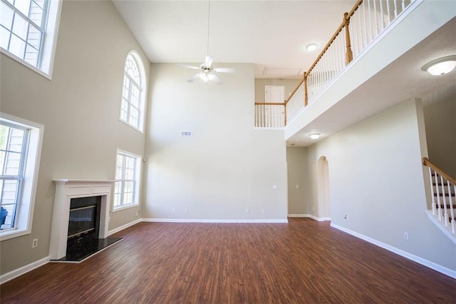 unfurnished living room featuring visible vents, a towering ceiling, wood finished floors, ceiling fan, and a high end fireplace