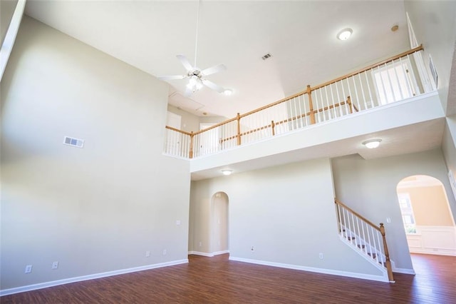unfurnished living room with a ceiling fan, wood finished floors, arched walkways, a towering ceiling, and visible vents