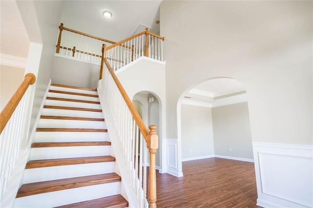 stairway featuring arched walkways, wood finished floors, and a high ceiling