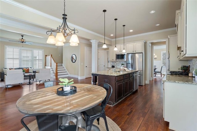 dining space featuring sink, crown molding, dark wood-type flooring, ceiling fan, and decorative columns