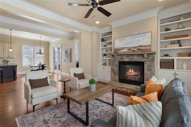 living room with ornamental molding, a stone fireplace, built in features, and dark hardwood / wood-style flooring