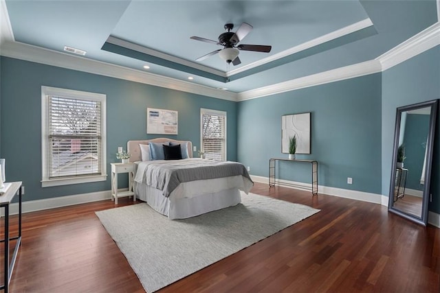 bedroom with dark wood-type flooring, ceiling fan, ornamental molding, and a tray ceiling