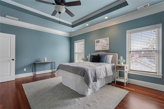 bedroom with dark wood-type flooring, ornamental molding, a raised ceiling, and ceiling fan